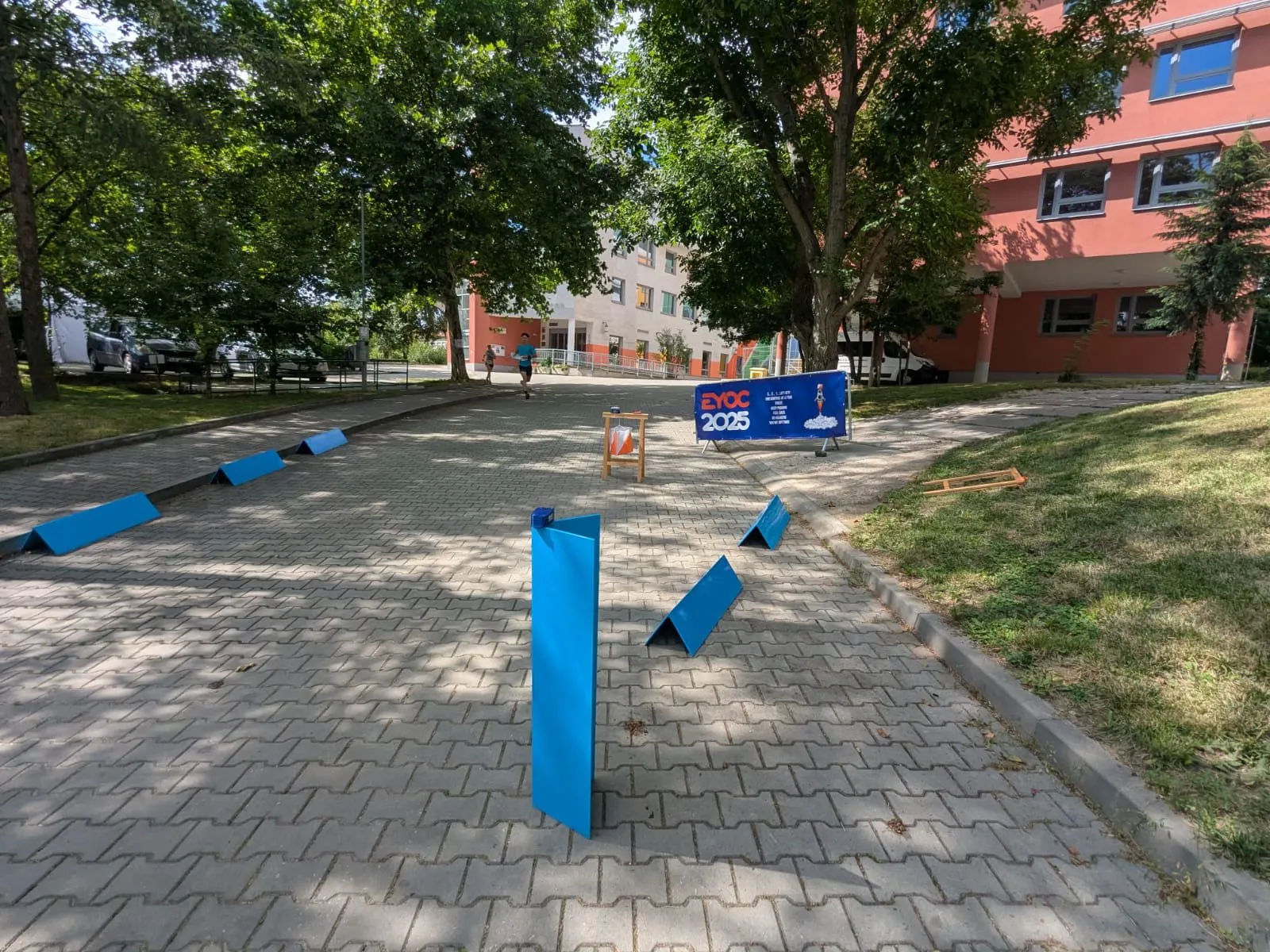 A run-through control on a path at EYOC 2025, with the Bluebox on an upright board a few meters behind the control and barriers guiding the runners past it